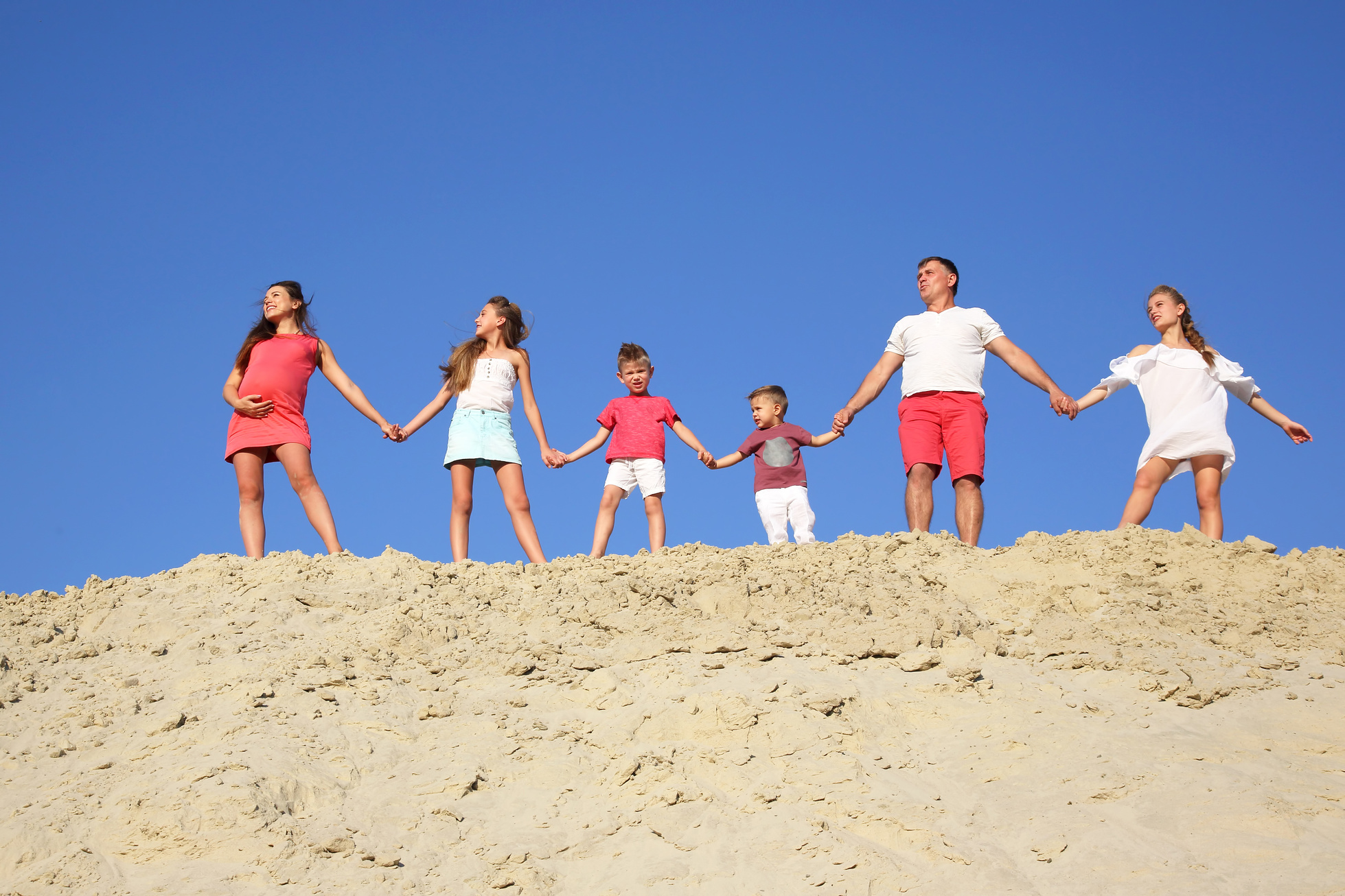 family with children stands holding hands on a sandy hill